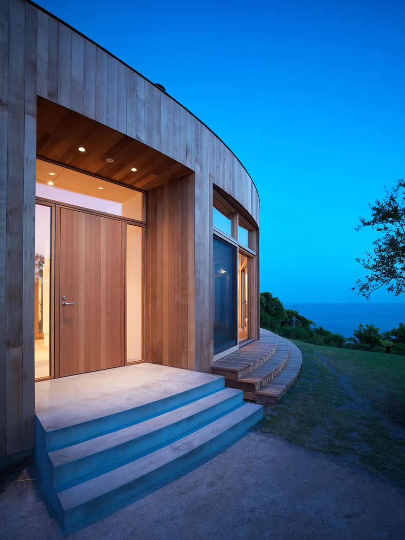 Recessed timber-lined entrance with concrete steps and curved bench at dusk overlooking hillside