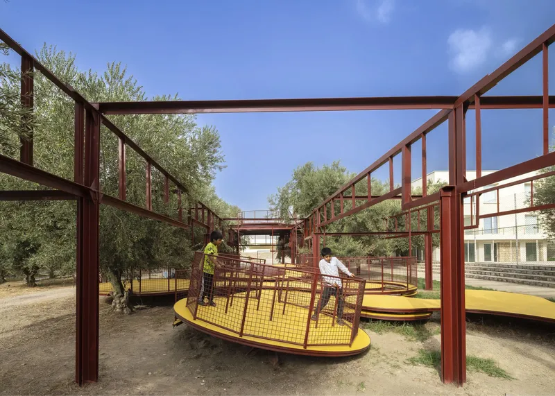 Red steel frame structure with yellow platforms weaving between olive trees under a clear blue sky