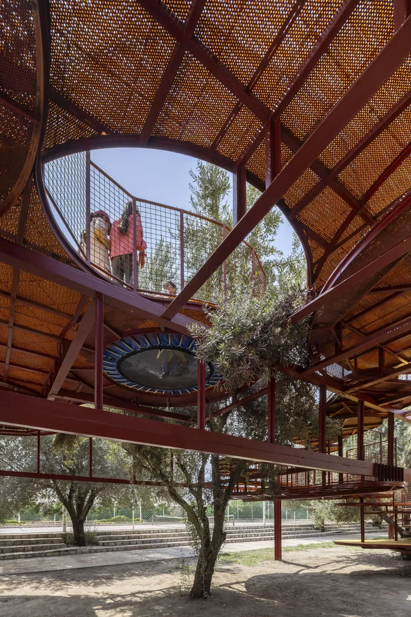 View from below the perforated metal canopy with steel frame looking up to a walkway where a figure stands