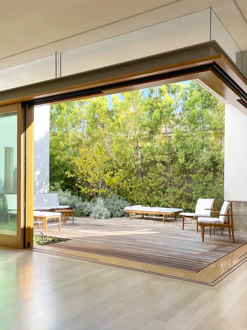 Wide sliding door opening from interior to timber deck terrace with trees in background