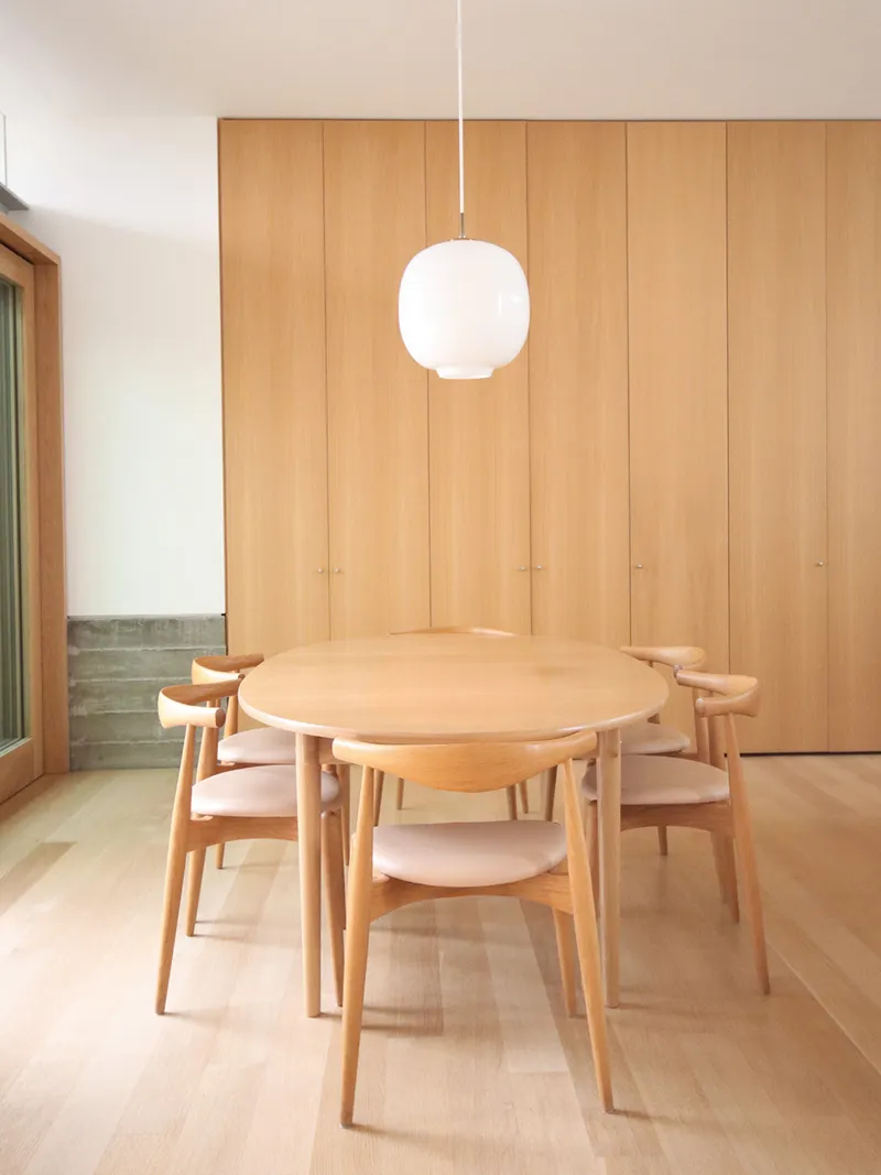 Dining room with round timber table and pendant light against floor-to-ceiling wood paneling
