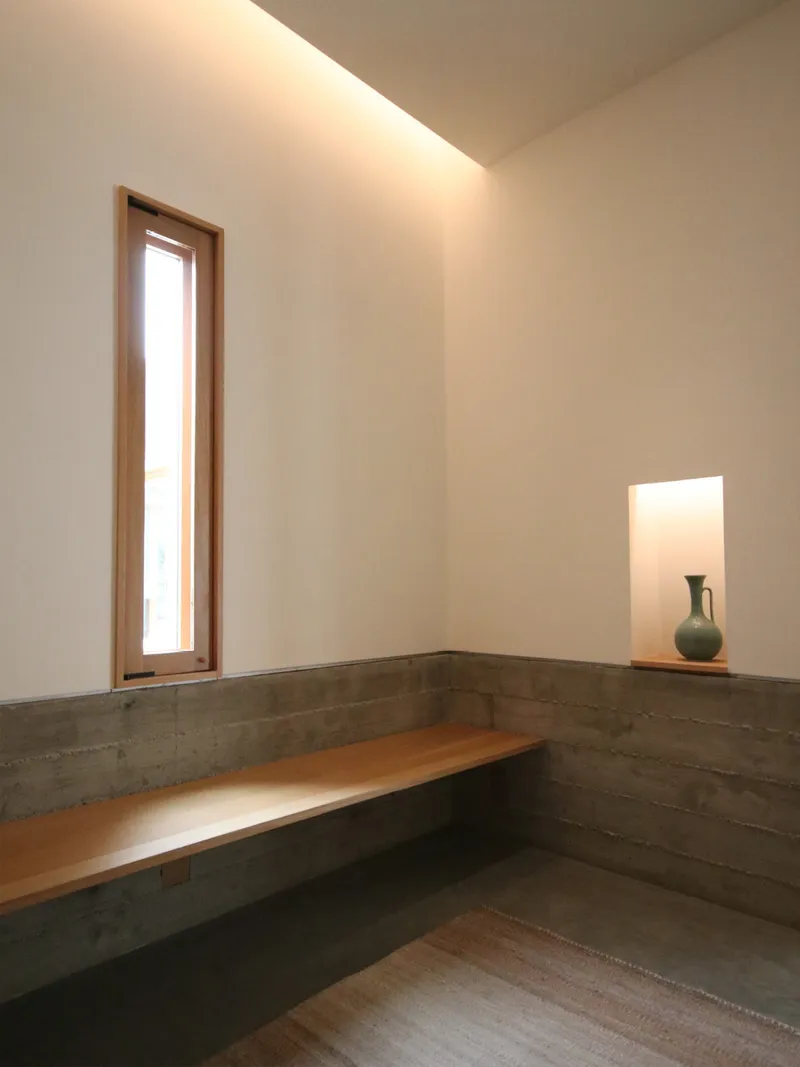 Seating nook with board-formed concrete bench and narrow timber window with ceramic vase