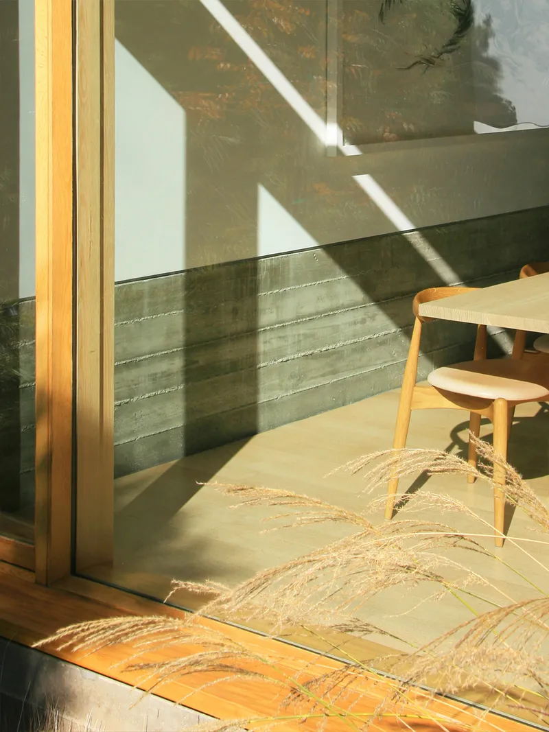 Glass door with timber frame casting diagonal shadows onto a board-formed concrete wall
