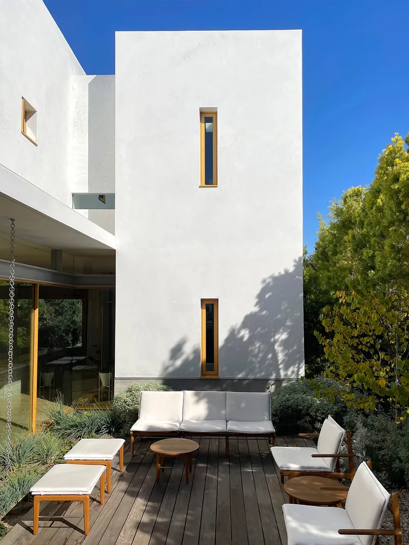 Outdoor terrace with timber lounge furniture beneath a white stucco facade with vertical slot windows