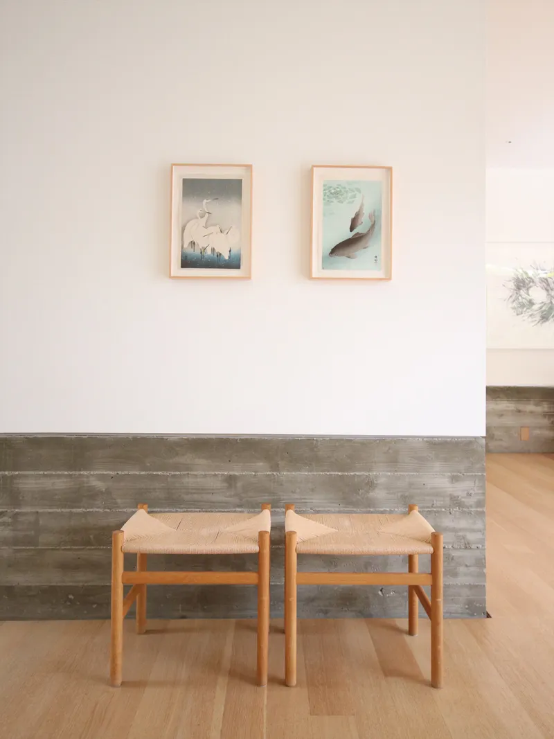 Two timber stools against a reclaimed wood wainscot below framed artworks on white wall