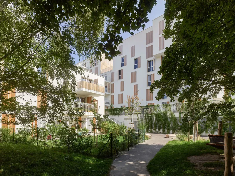 White residential blocks with timber shutters framed by mature trees and a garden pathway in summer