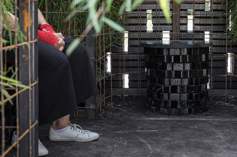 Interior view through woven brick walls with openings filtering light and vegetation visible outside