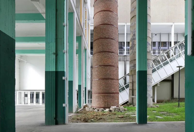 View through green-painted columns toward a preserved brick chimney and planted courtyard area