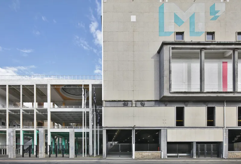 Street elevation showing precast concrete panels with blue graphic motifs beside a glazed white frame structure