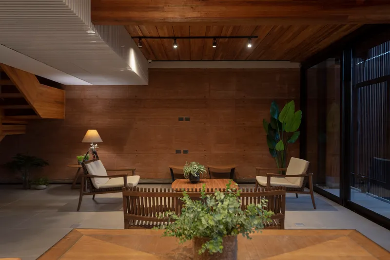 Interior courtyard with timber ceiling, rammed earth walls, potted plants, and upholstered seating at night