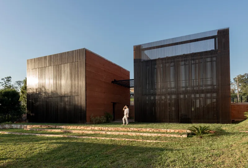 Frontal view of corrugated metal screen and rammed earth volumes in low afternoon sun