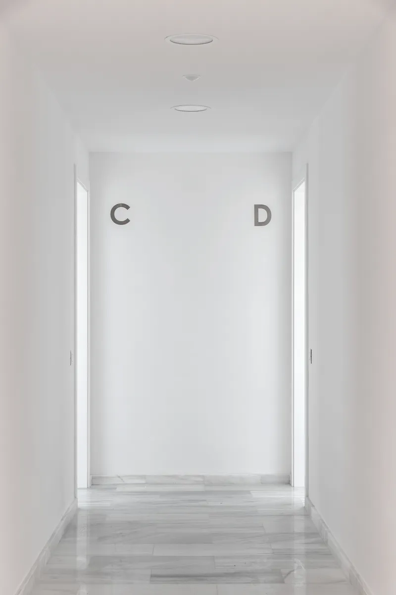White corridor with pale timber flooring leading to a backlit wall marked with letters C and D