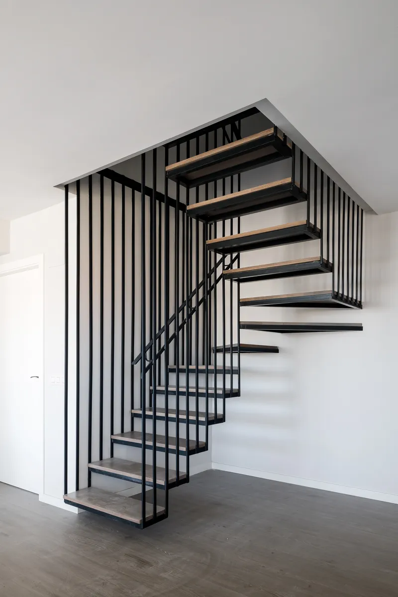 Black steel and timber staircase with vertical rod balustrade ascending through a white interior
