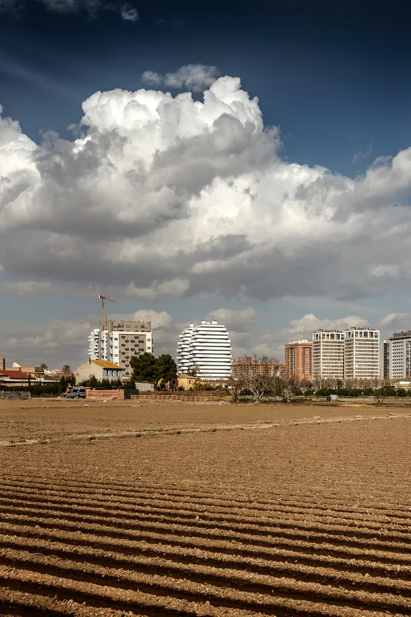 Distant view of the cylindrical tower with horizontal banding across a sandy beach under dramatic clouds