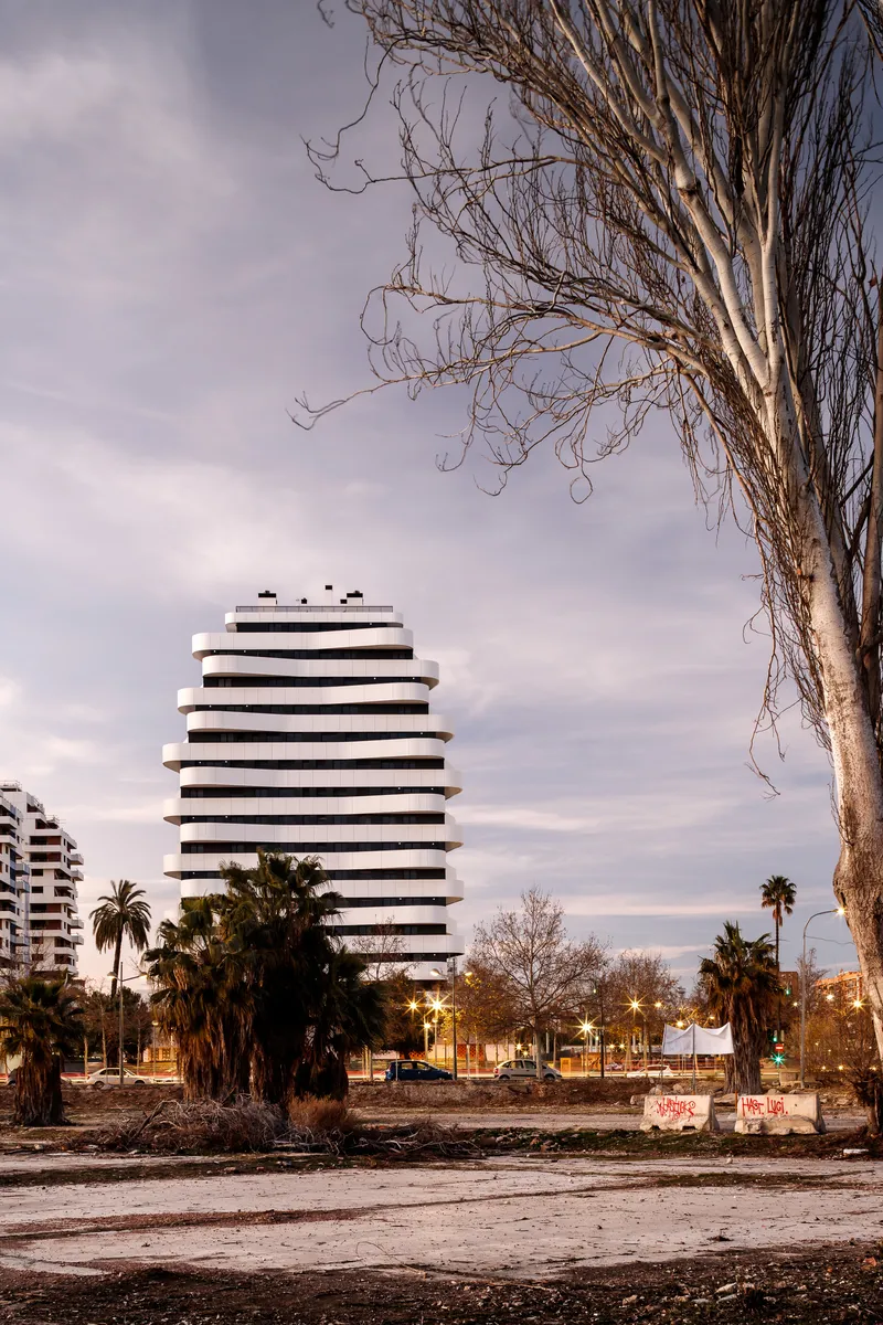 Distant view of the horizontally banded tower facade framed by a bare tree in late afternoon light