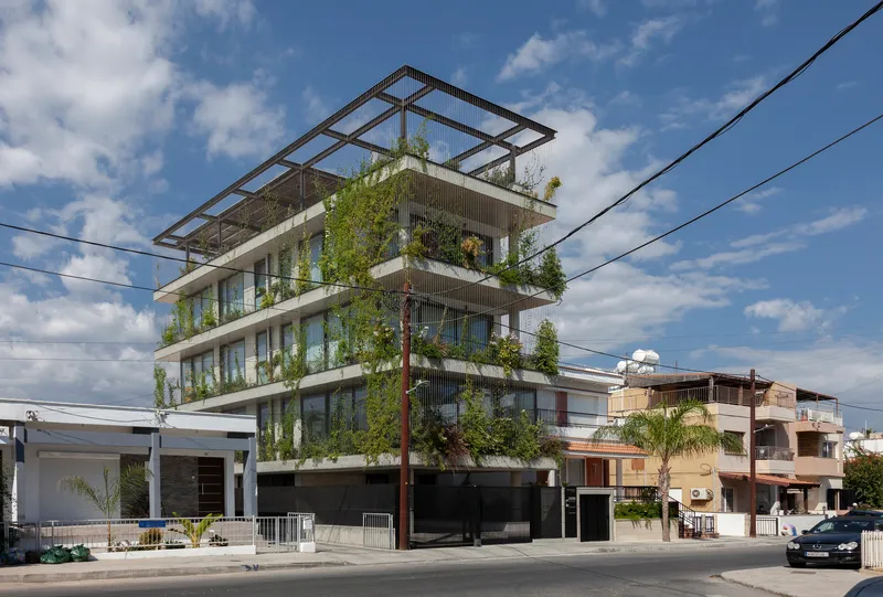 Street view of the five-story facade with planted balconies and a rooftop pergola under clouds