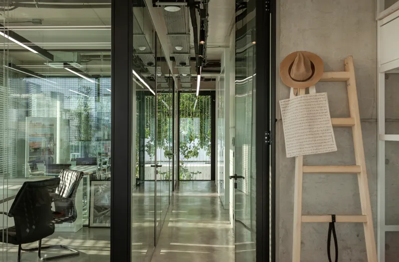 Glass corridor with black steel frames looking toward an interior courtyard with hanging plants