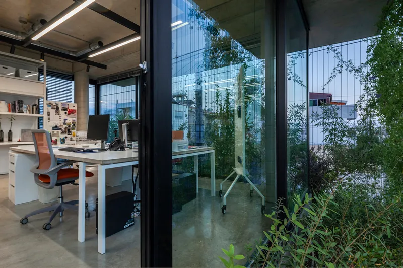 Office workstation beside floor-to-ceiling glazing overlooking a planted terrace with climbing vines
