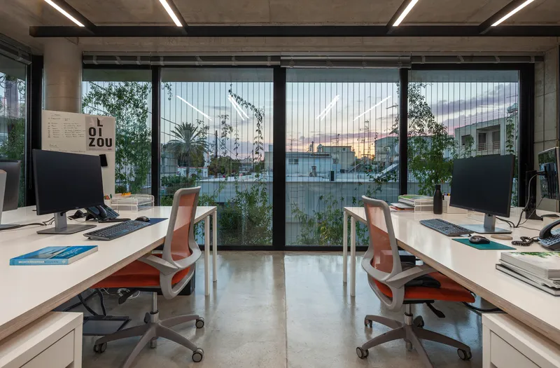 Pair of workstations facing full-height glazed facade with view of planted terrace at dusk