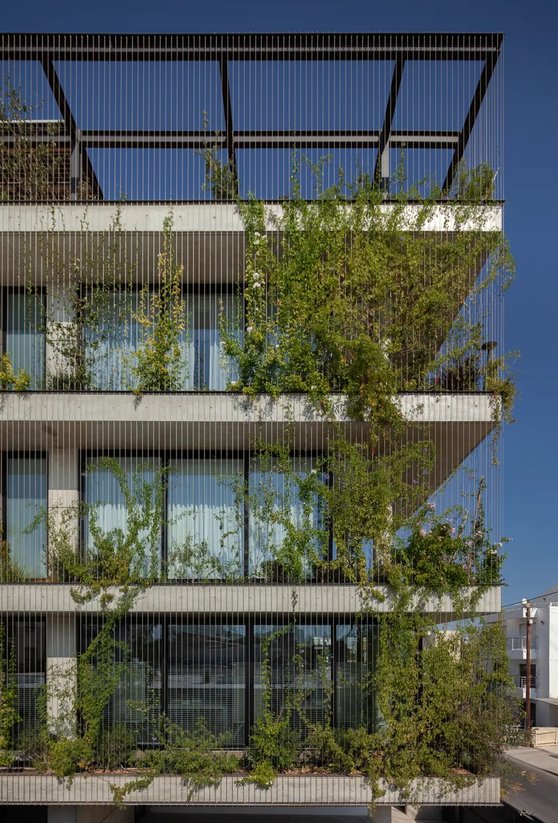 Close view of the layered facade with climbing vegetation behind the vertical metal louvers