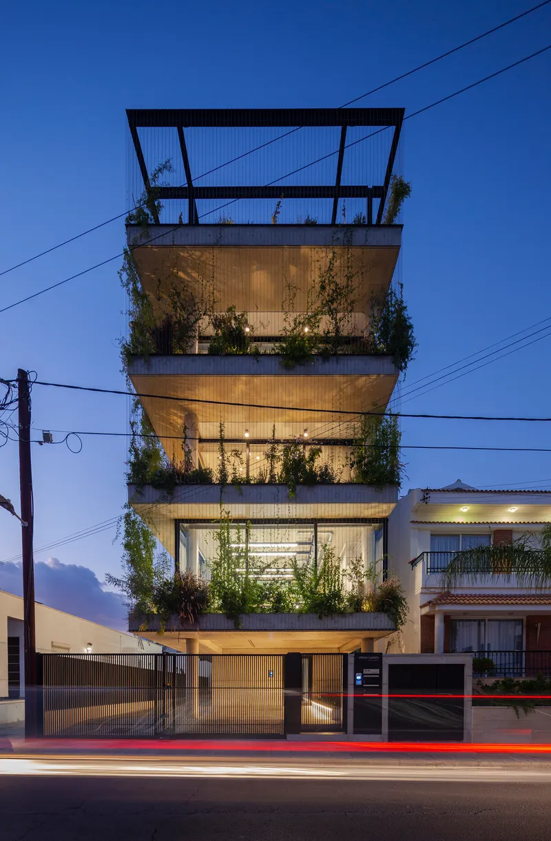 Street view of a four-story concrete facade with planted balconies at dusk with car light trails
