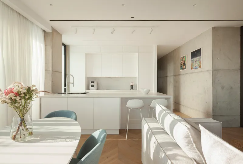 Open-plan kitchen and dining area with white cabinetry and concrete wall panels under soft daylight