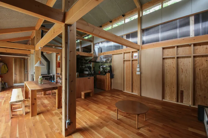 Dining area with timber posts, beams, and plywood storage panels beneath high clerestory glazing