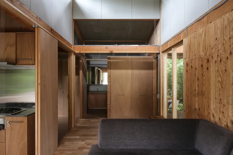 Interior passage framed by timber structure showing plywood wall panels and a view through to other rooms