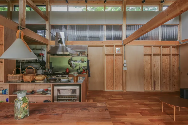 Open kitchen with exposed timber beams, clerestory windows and corrugated metal wall panels above plywood cabinetry