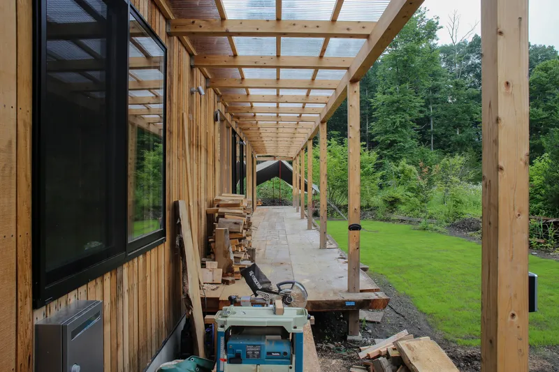 Covered timber walkway with translucent roof panels overlooking a lawn and forest edge