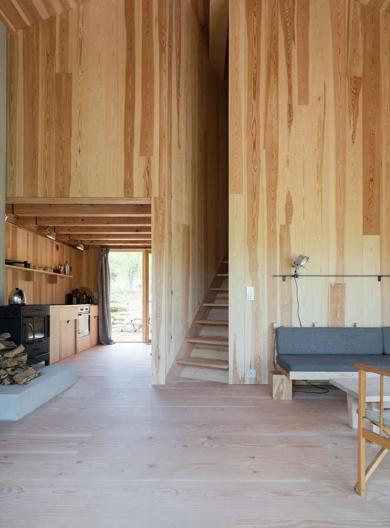 Double-height interior with vertical timber paneling, open kitchen, and staircase leading to upper level