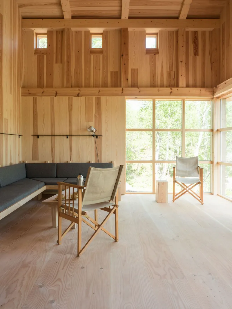 Living area with exposed timber beams, clerestory windows, and paired canvas chairs facing glazed wall