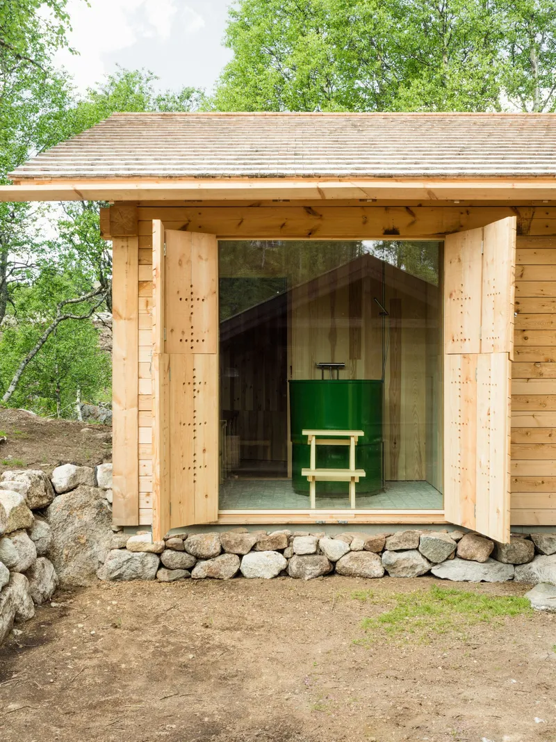 Timber pavilion with open double doors revealing a green bench and fieldstone foundation wall