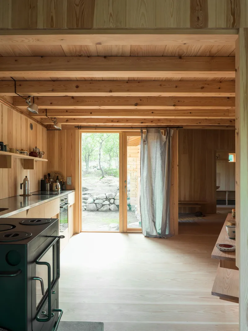 Kitchen with exposed ceiling beams and glazed door framing a view to the stone landscape outside