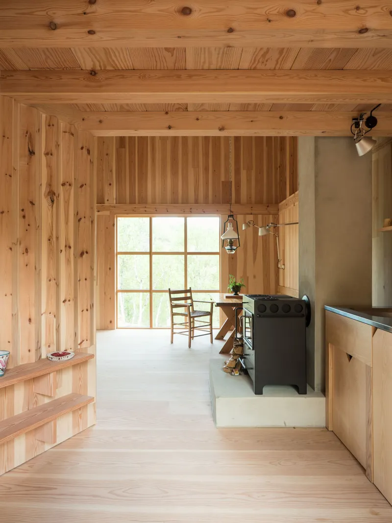 Interior with wood-lined walls and ceiling, large gridded window and wood-burning stove in the corner