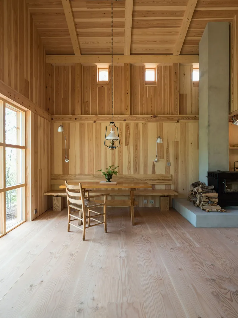 Dining area with pendant lights suspended above a table and concrete fireplace hearth with stacked firewood