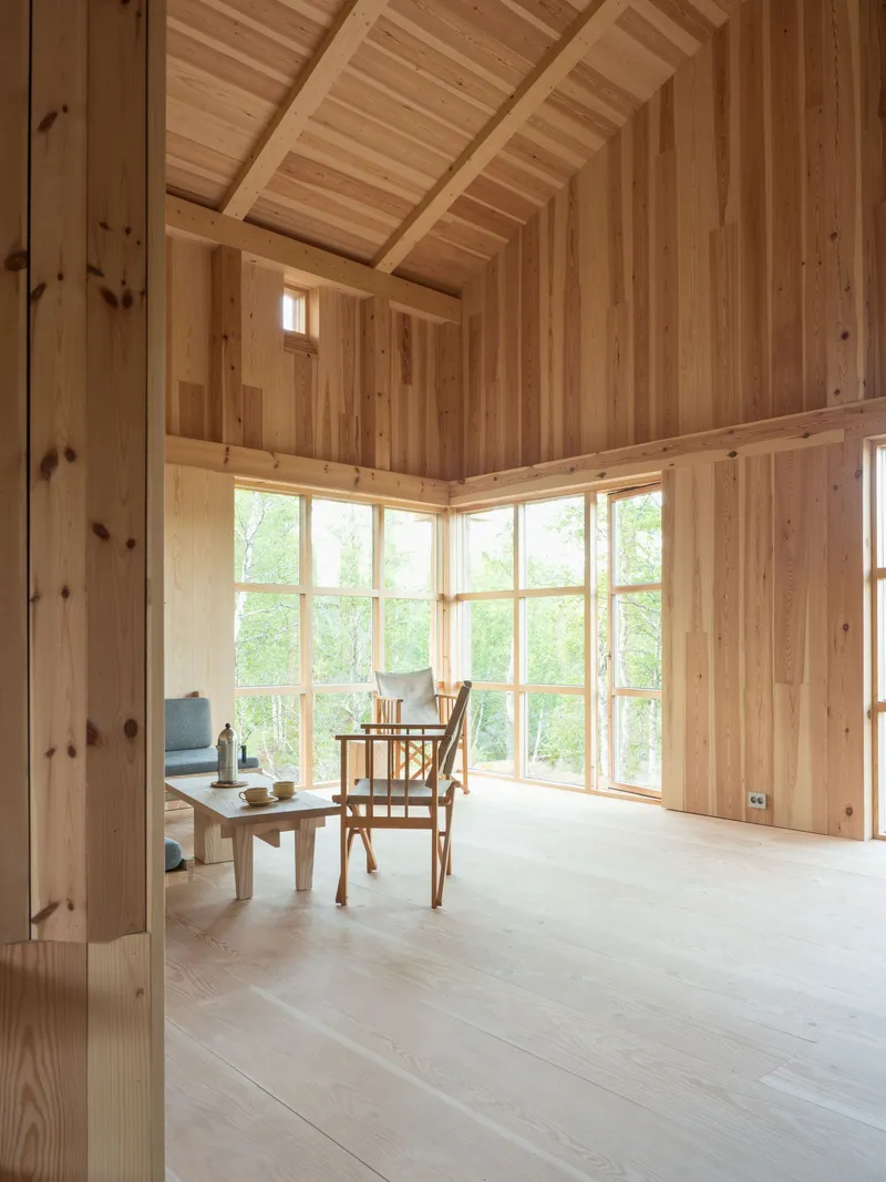 Corner room with angled timber ceiling and floor-to-ceiling windows overlooking birch trees in summer