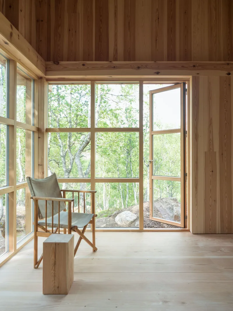 Canvas chair beside a timber stump and open casement window looking out to the rocky woodland