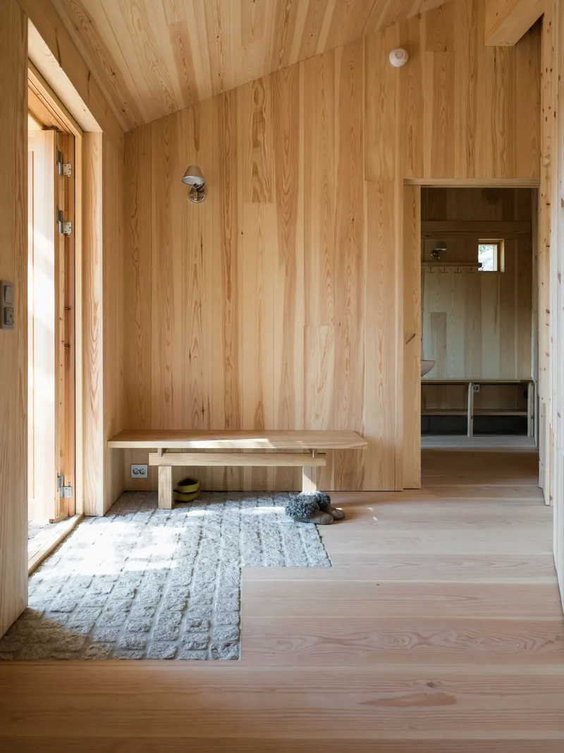 Timber-lined entryway with built-in bench, textured rug, and view through to interior room beyond