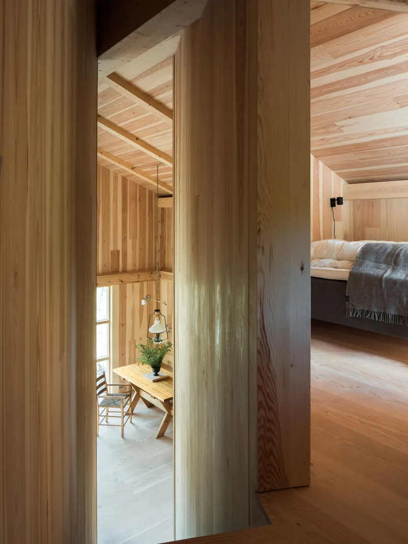 View through vertical wood columns toward dining area with hanging pendant and bedroom in background