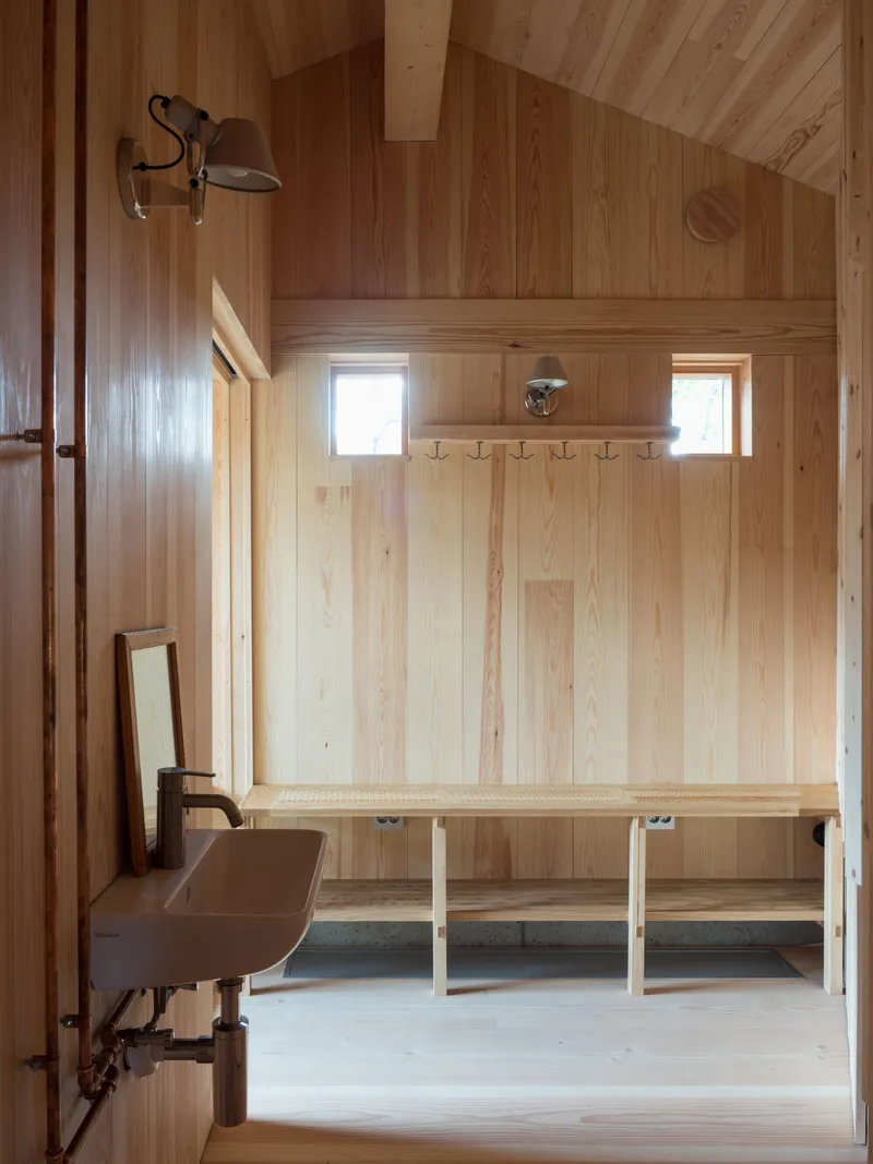 Mudroom with wall-mounted coat hooks, continuous bench, twin square windows, and concrete floor