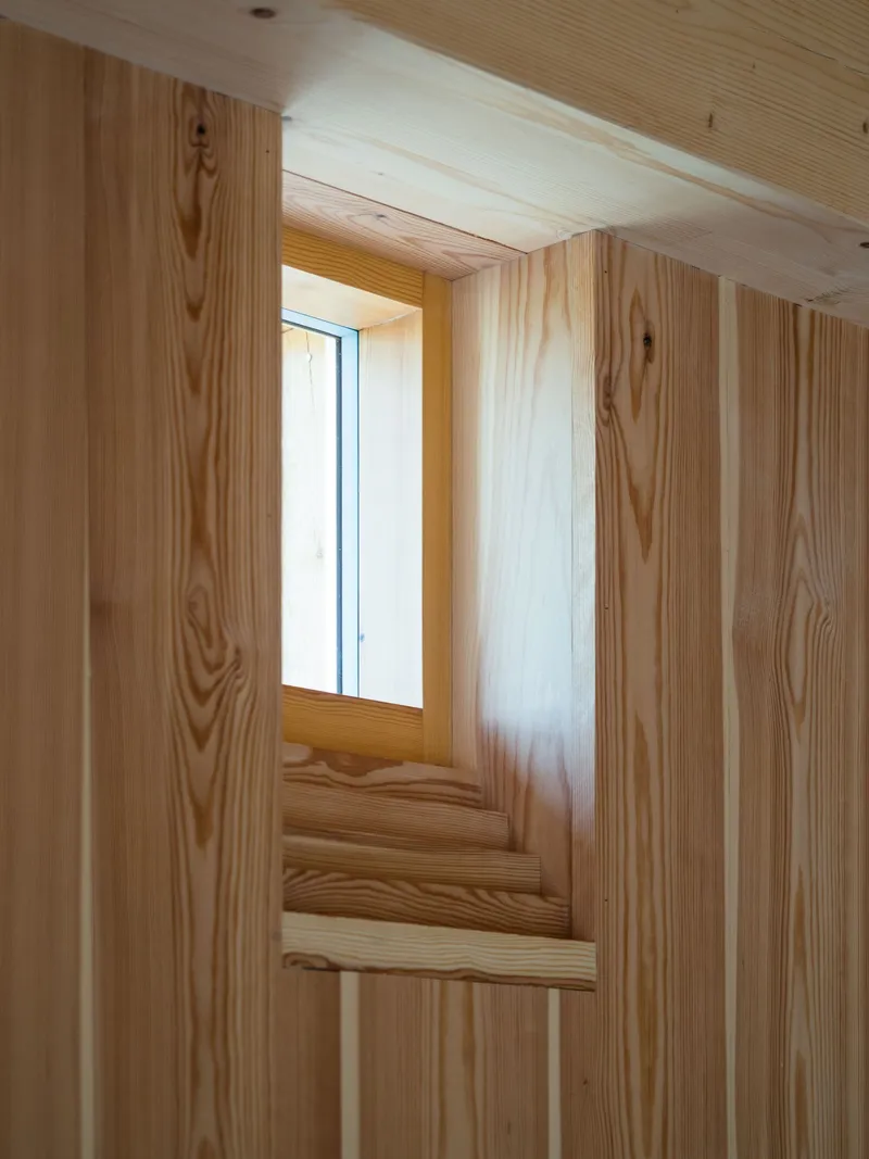 Detail of recessed window niche framed in layered wood planks showing natural grain variation