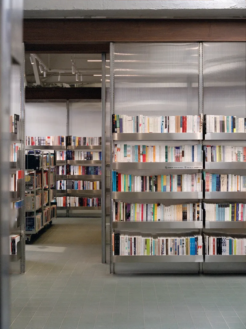 Metal shelving unit with books reflected in translucent corrugated panel dividers under exposed timber beams