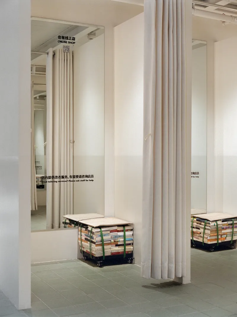 White curtain divider beside seating cube made from stacked recycled books on a wheeled base beneath mirrored panels
