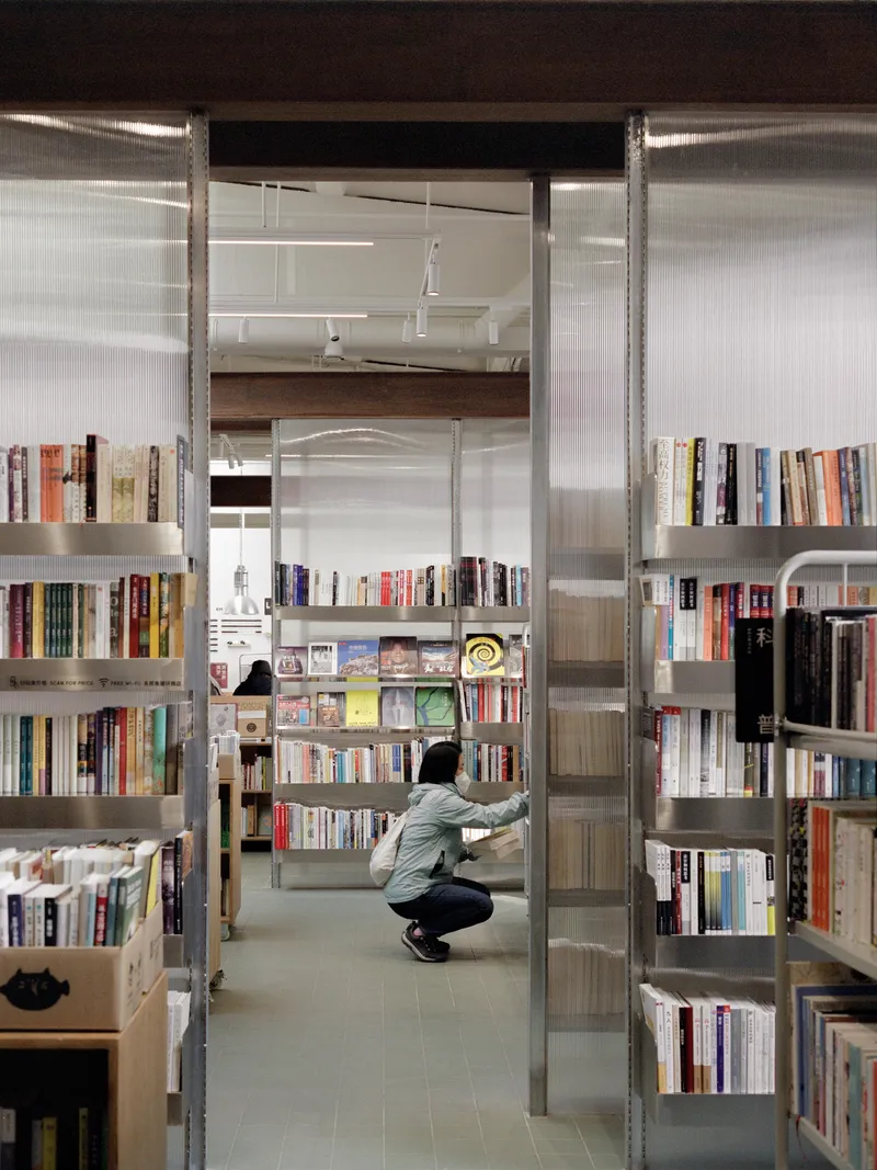 View through metal shelving units into the bookstore with a visitor crouching among the stacks