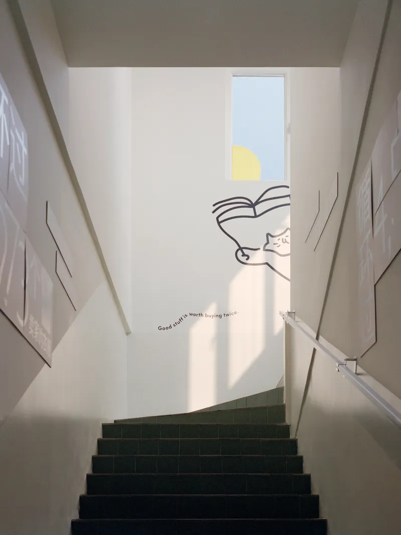 Stairwell with green tile treads and sunlight streaming through a high window above mural graphics