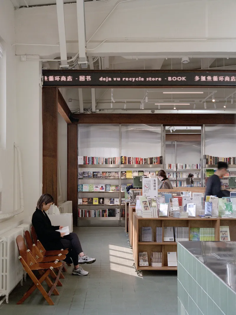 Interior reading area with exposed white ceiling structure and timber-framed bookshelves beyond folding chairs
