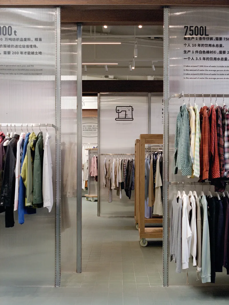 Clothing racks suspended from galvanized steel frames with translucent panels and graphic signage above