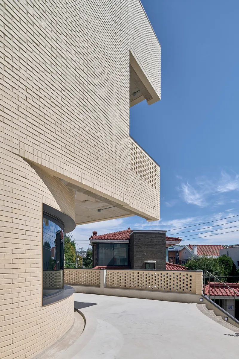 Curved terrace with horizontal white brick facade and perforated parapet wall under clear blue sky