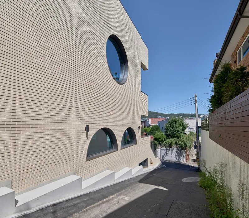 Street view of white brick facade with circular and arched windows along a narrow lane